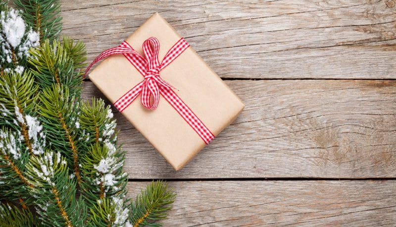 Kuva lahjapaketista puisella alustalla, jonka vierellä on lumisia kuusenoksia.