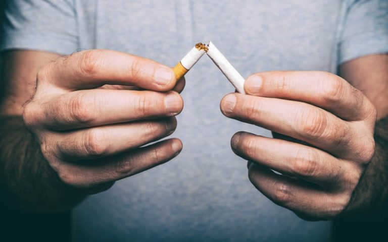 Lähikuvassa miehen kädet katkaisevat savukkeen kahtia.