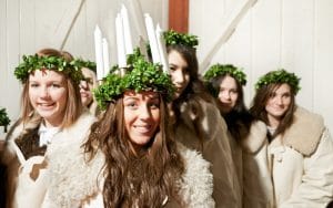 Lucia kulkee etunenässä vihreään lehvään tehdyssä kruunussa ja valkoisissa kynttilöissä, seuranaan jouluperinteeseen kuuluvat saattohahmot.