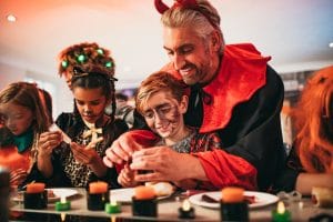 Halloween-asuun pukeutunut aikuinen opastaa lapsia tekemään itse halloween-henkisiä esineitä.