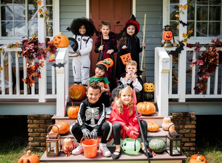 Kuva lapsijoukosta halloween-asuissa talon edustalla, jonka terassi on halloween-teemalla koristelu.