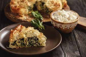 Etualalla viipale börek-feta-pinaattipiirasta ruskealla lautasella ja taustalla piirakka, josta viipale on leikattu.