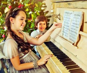 Tyttö soittaa pianoa ja laulaa pikkuveljensä kanssa joululauluja.
