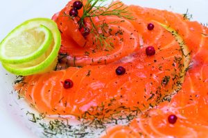 Lähikuva graavatusta lohesta, jonka päällä on rosepippureita ja tilliä. Nurkassa on myös limettikukka.