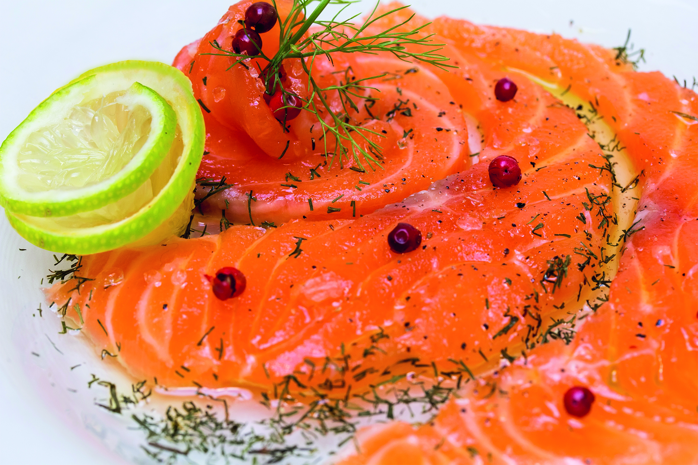 Lähikuva graavatusta lohesta, jonka päällä on rosepippureita ja tilliä. Nurkassa on myös limettikukka.