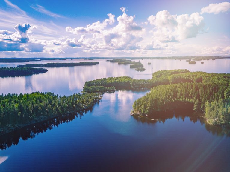 Ilmakuva sinisistä järvistä ja vihreistä metsistä kesäisessä Suomessa.