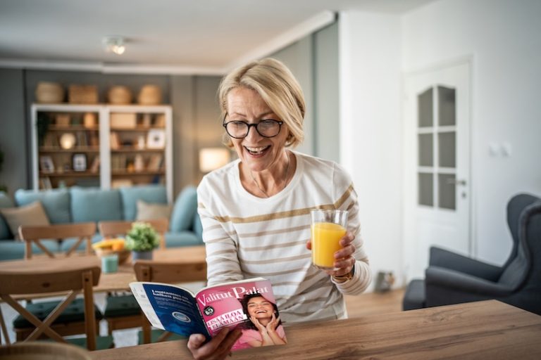 Vanhempi nainen istuu kotoisan keittiön työtason äärellä ja hymyilee leveästi lukiessaan Valitut Palat -lehteä. Lehden kannessa lukee "Lisää iloa elämään".